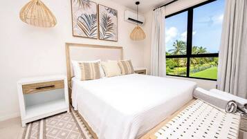 A bedroom with a large bed, a nightstand, a window with a view of greenery, and two pendant lights.