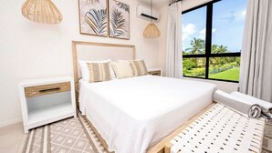 A bedroom with a large bed, a nightstand, a window with a view of greenery, and two pendant lights. - Azzurro Townhouses - by Zenbreak (Speightstown)