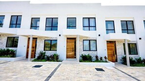 A modern multi-story building with a symmetrical facade, large windows, and a central entrance with a wooden door. - Azzurro Townhouses - by Zenbreak (Speightstown)