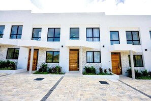 A modern multi-story building with a symmetrical facade, large windows, and a central entrance with a wooden door. - Azzurro Townhouses - by Zenbreak (Speightstown)