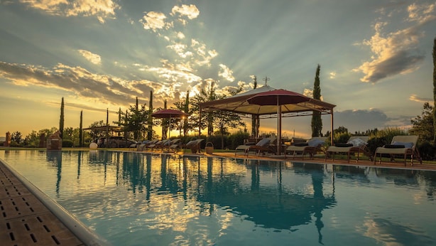 Zona de piscina con tumbonas y sombrillas, rodeada de árboles y un pabellón.