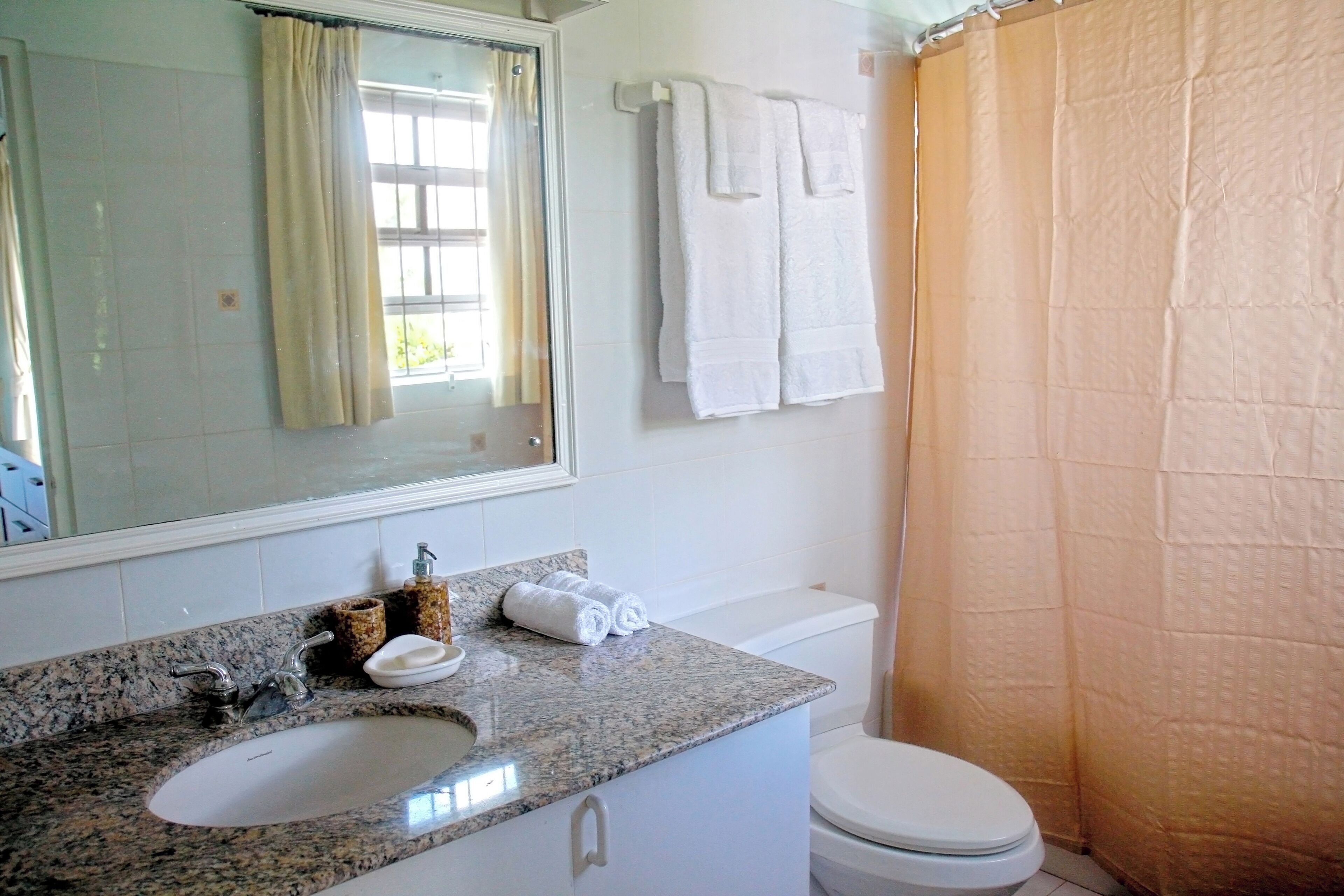 A bathroom with a granite countertop sink, a mirror, a toilet, and a shower curtain.
