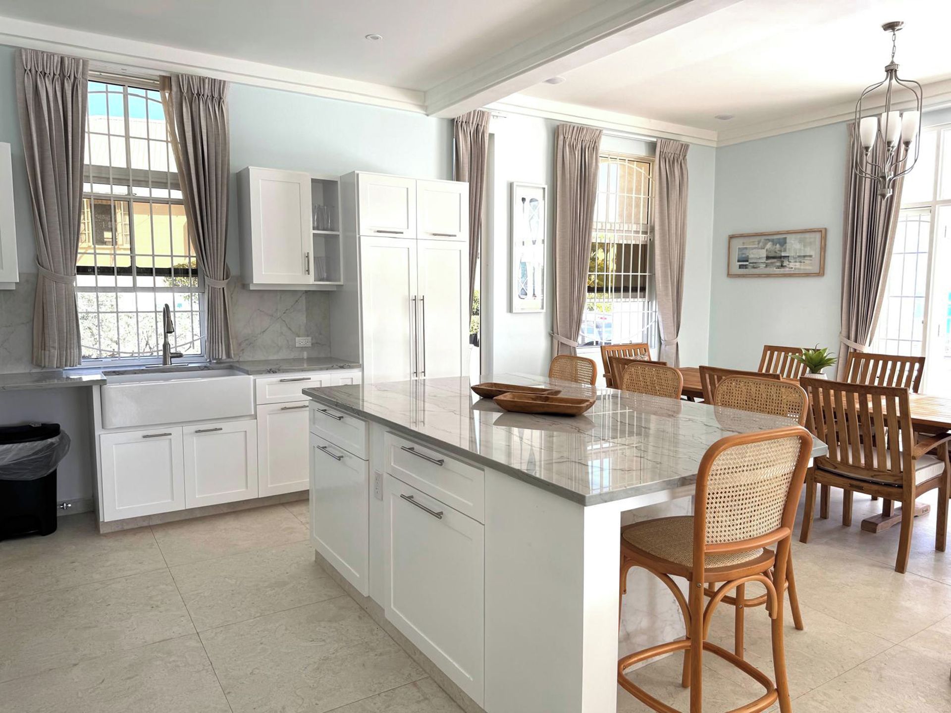 A modern kitchen with white cabinetry, a marble countertop, and a dining area with wooden chairs and a table.