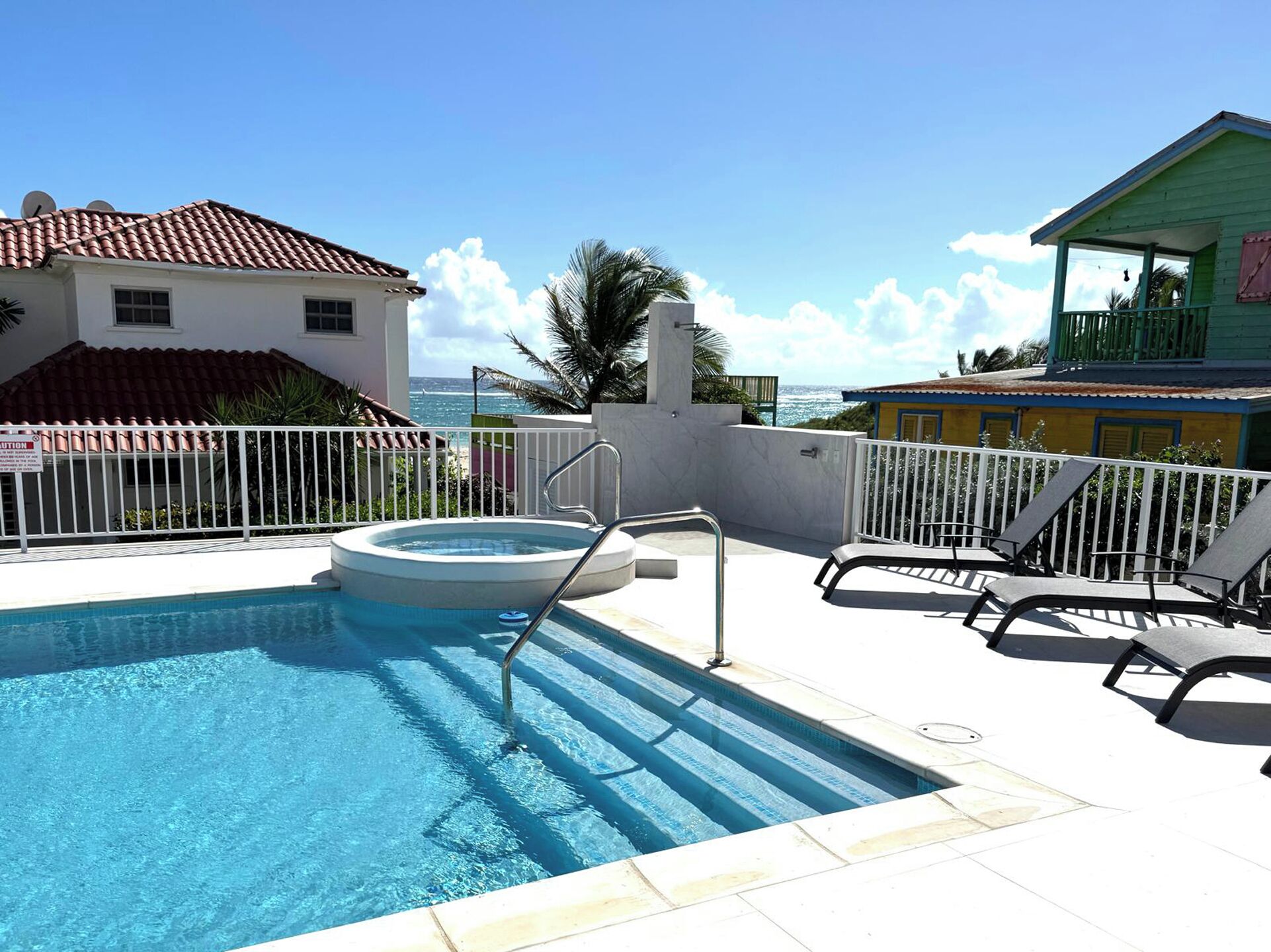 Piscina com vista para o oceano, uma pequena banheira de hidromassagem e uma área coberta com varanda.
