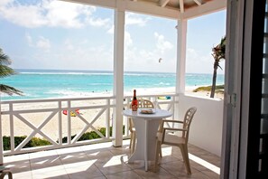 Een overdekt terras met een tafel en stoelen, met uitzicht op een strand en de oceaan.