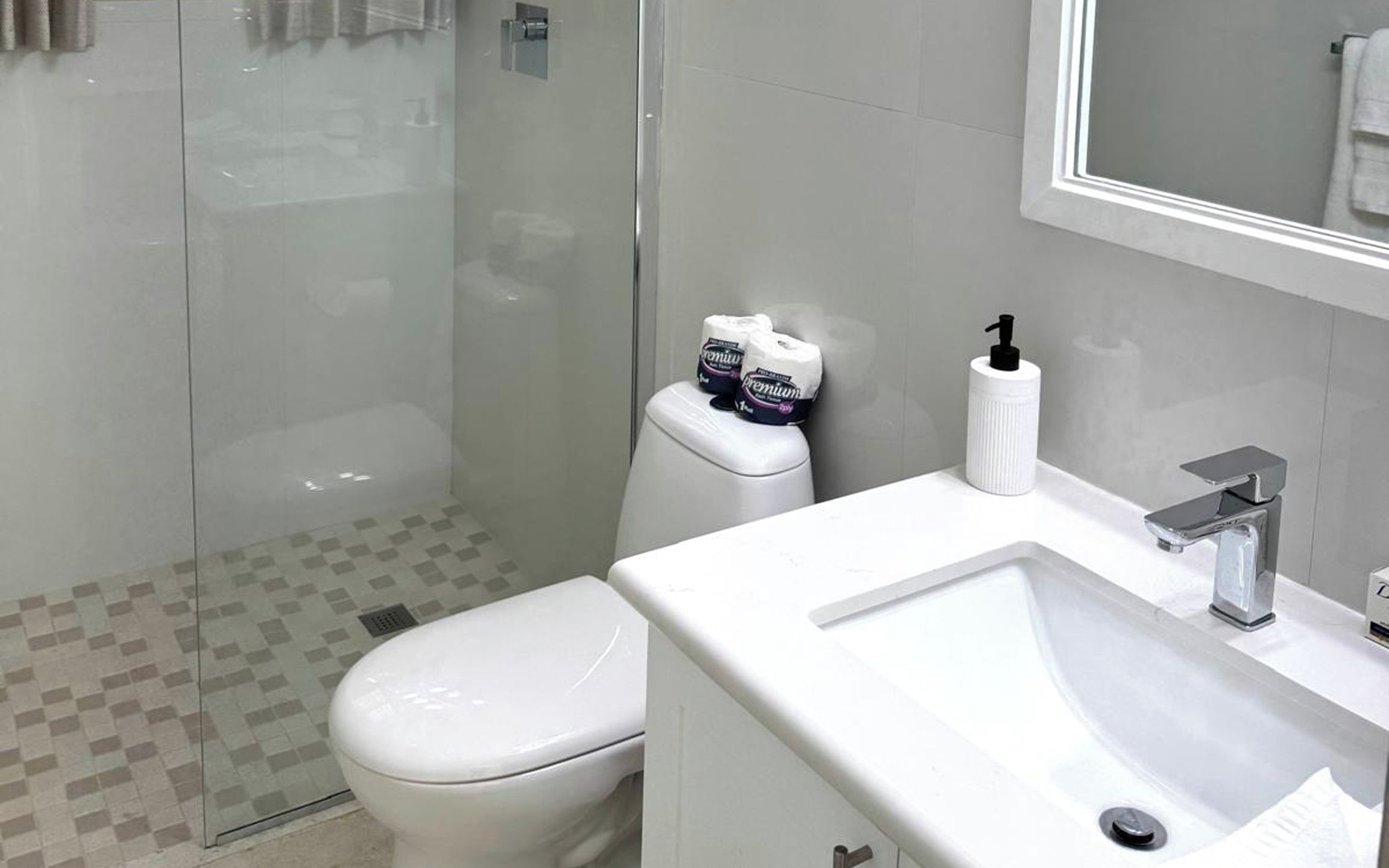 Une salle de bain moderne avec une douche à parois de verre, des toilettes blanches et un lavabo surmonté d’un miroir.