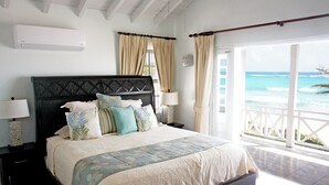 Un dormitorio con una cama grande, dos mesitas de noche, un velador y una ventana con cortinas, con vista al océano.