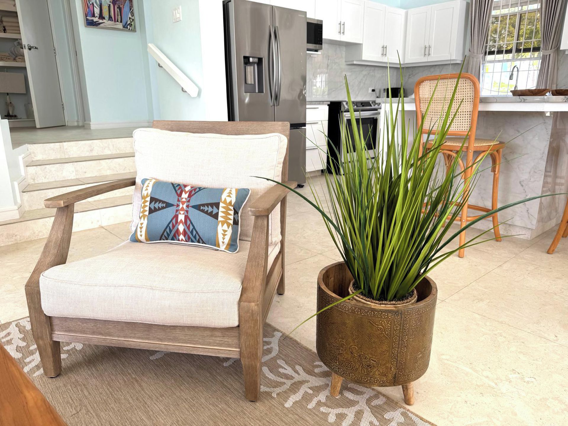 Una cocina moderna con armarios blancos, un refrigerador de acero inoxidable y una zona de comedor con una silla de madera y una planta en maceta.