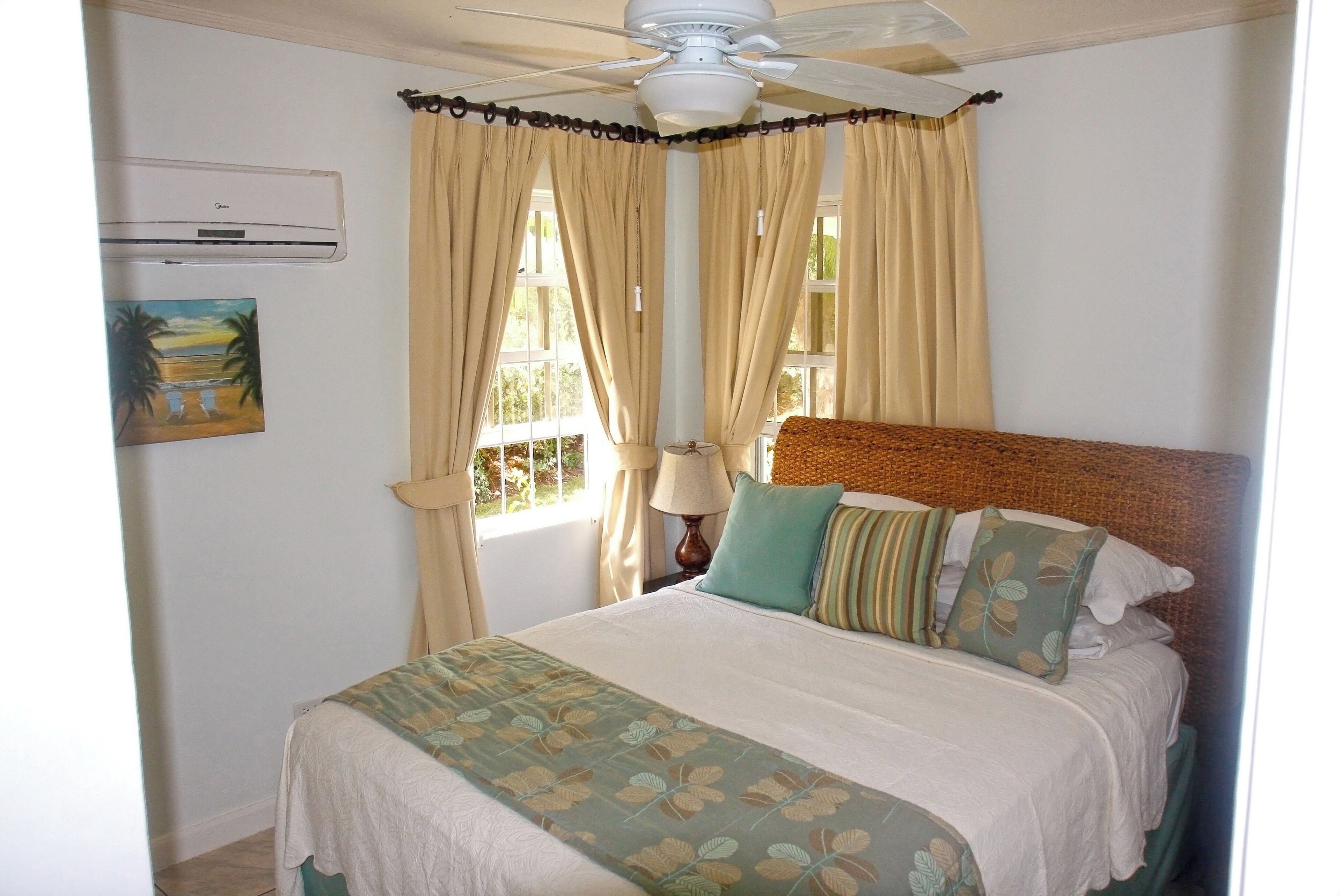A bedroom with a bed, curtains, a ceiling fan, an air conditioner, and a painting on the wall.