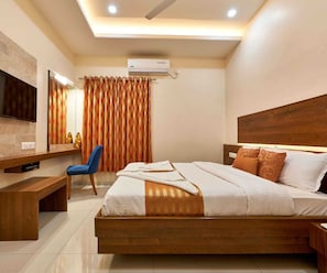 A modern hotel room with a large bed, a desk, a chair, a TV, and an air conditioning unit.