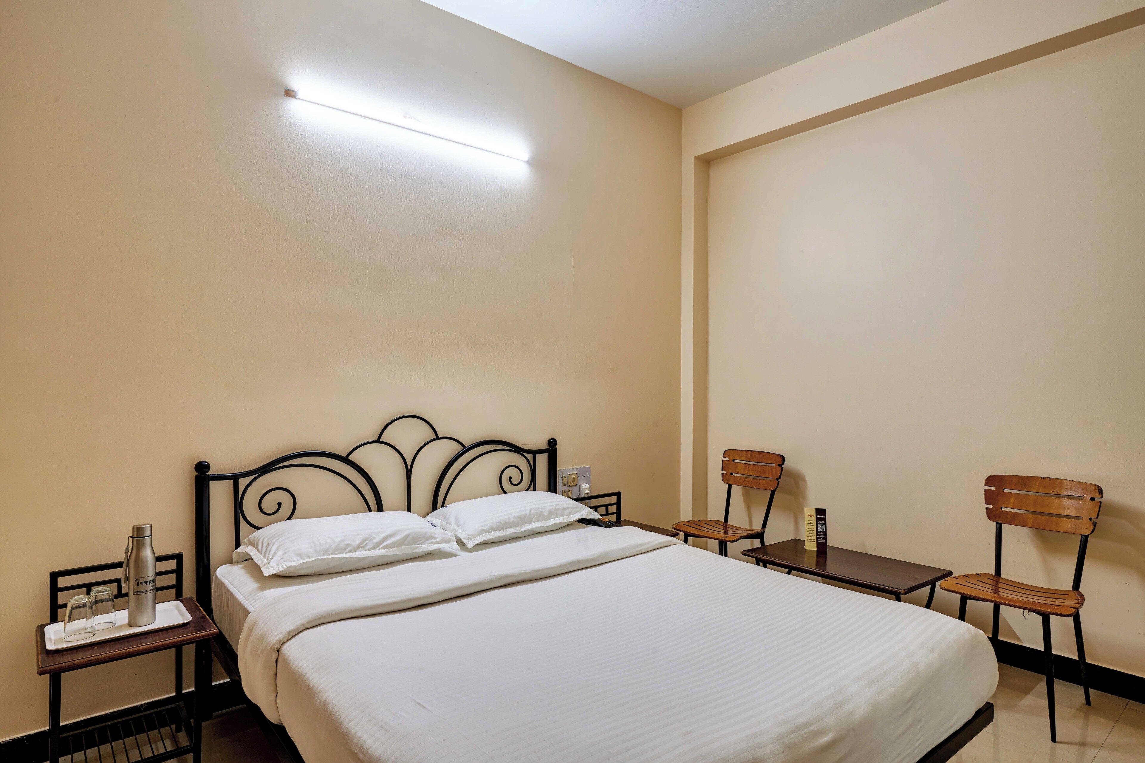 Een hotelkamer met een bed, nachtkastje, tafel, twee stoelen en een wandlamp.