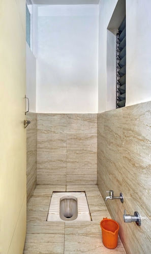 A small, modern bathroom with a minimalist design, featuring a toilet, a bucket, and a shower control.