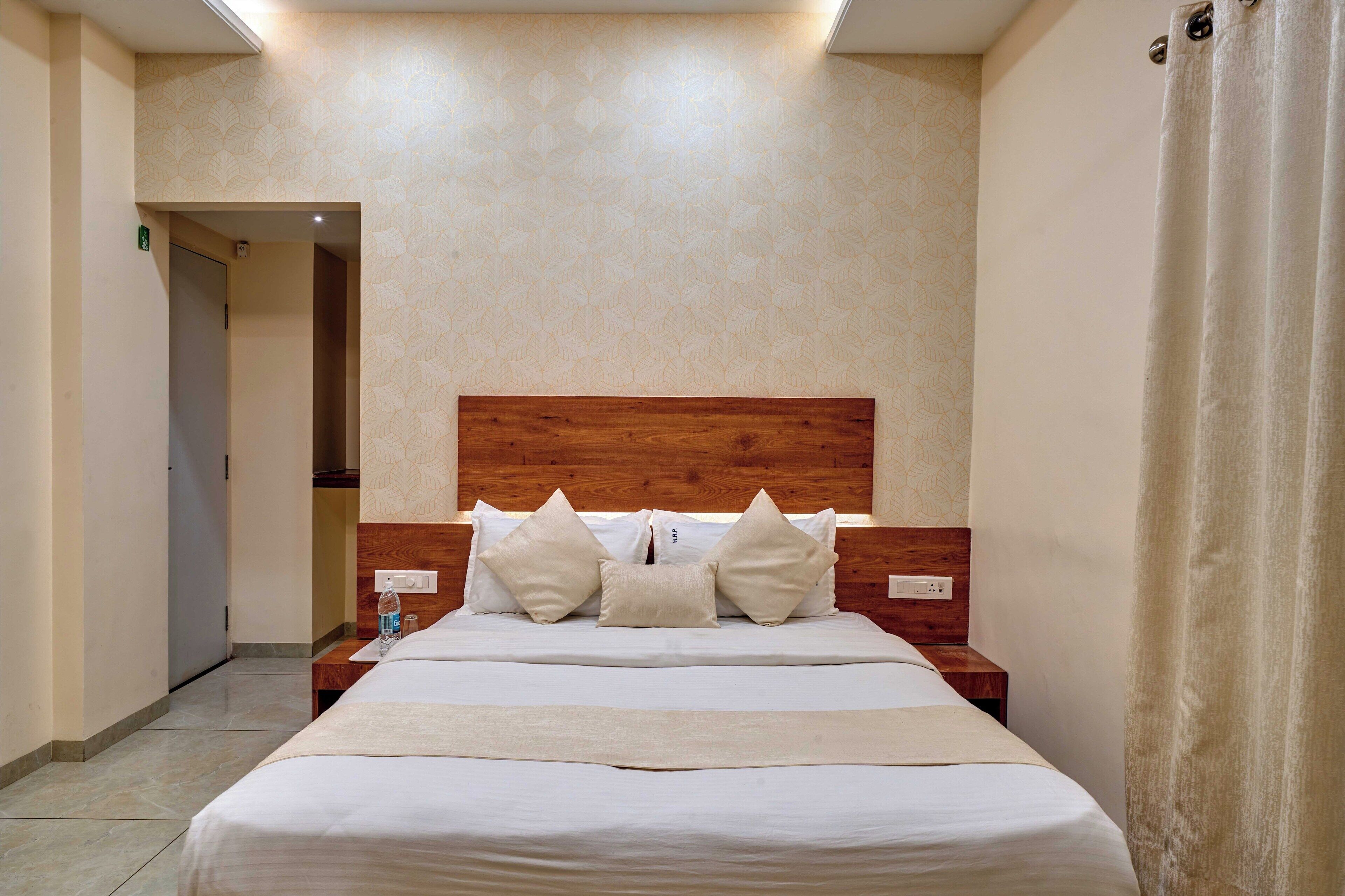 A hotel room with a wooden headboard, a large bed with white linens, two bedside tables, and a water bottle on one of the tables.