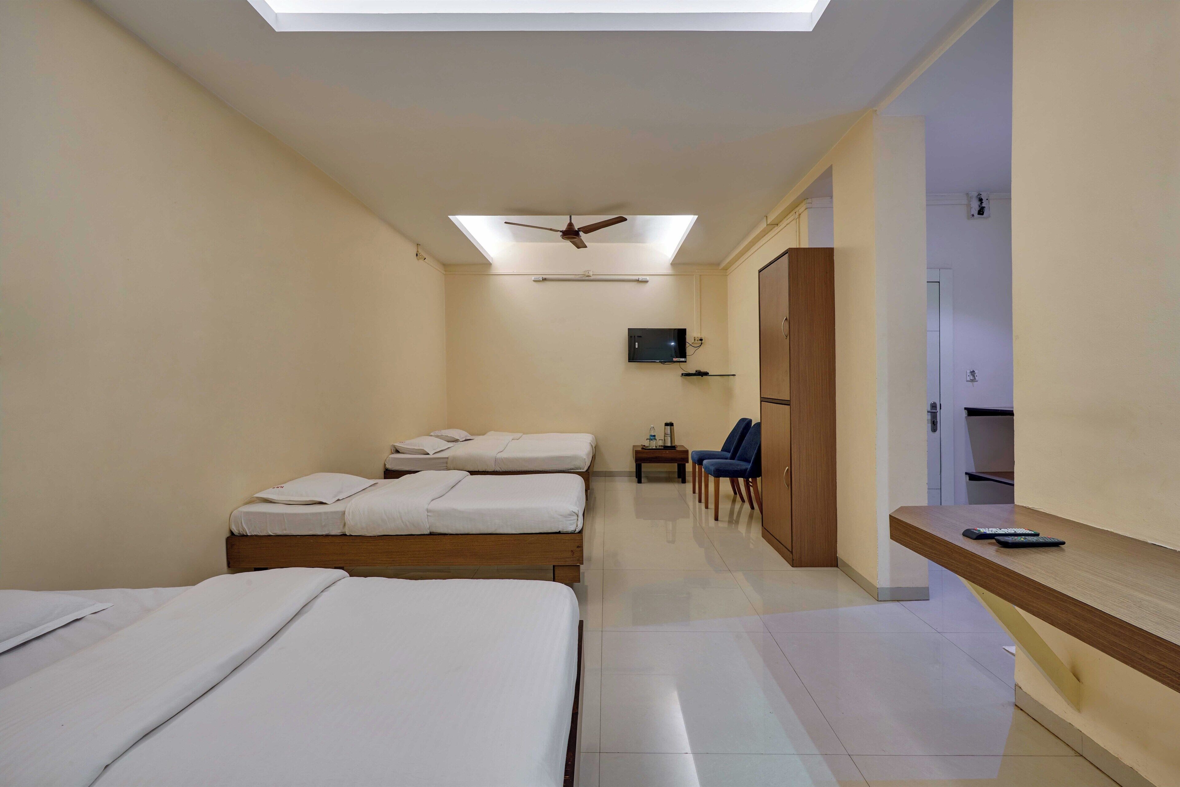 A hotel room with two beds, a TV, a desk, and a ceiling fan.