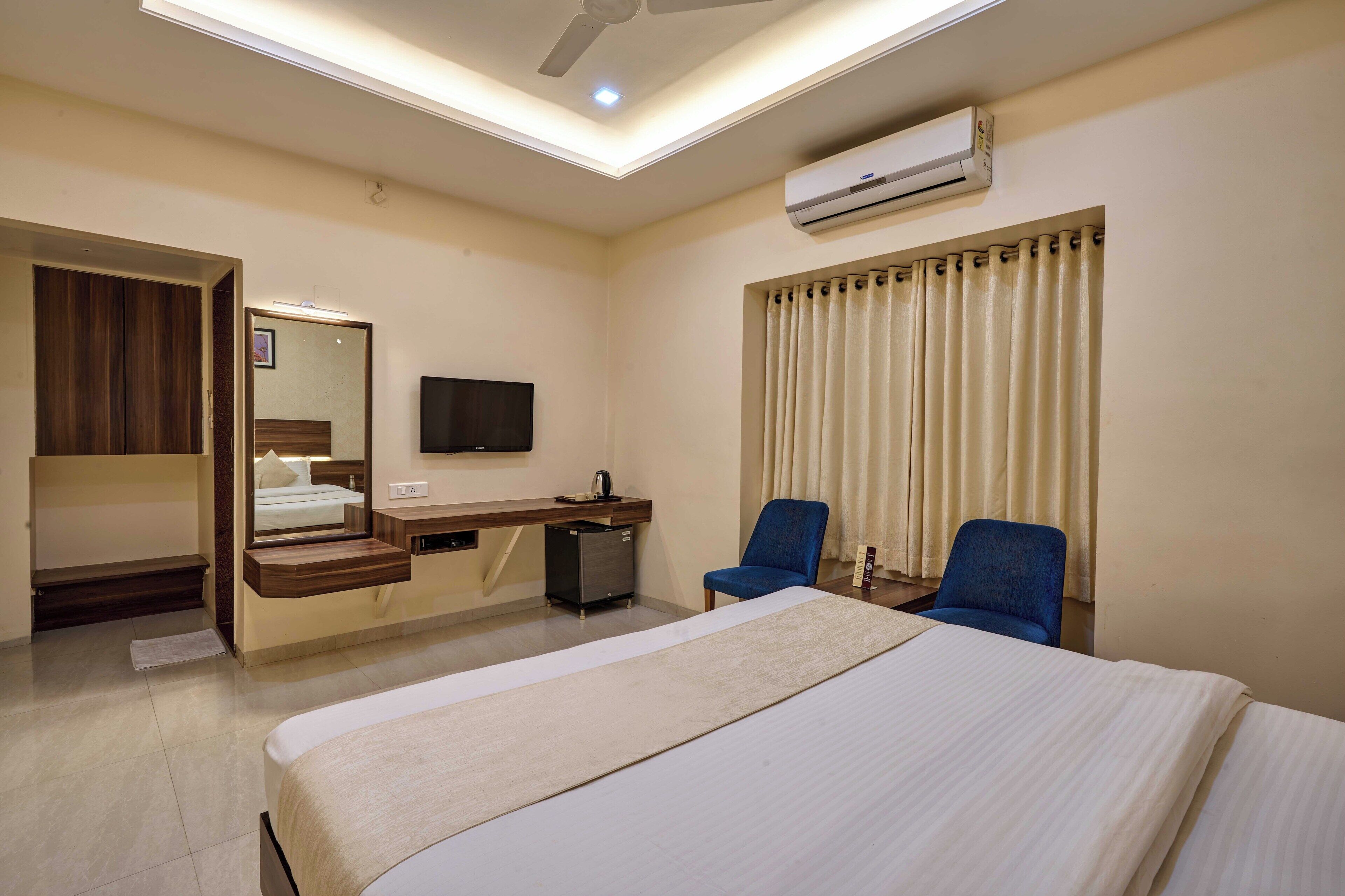 Habitación de hotel con cama, escritorio con computadora, silla, armario, televisor y aire acondicionado.