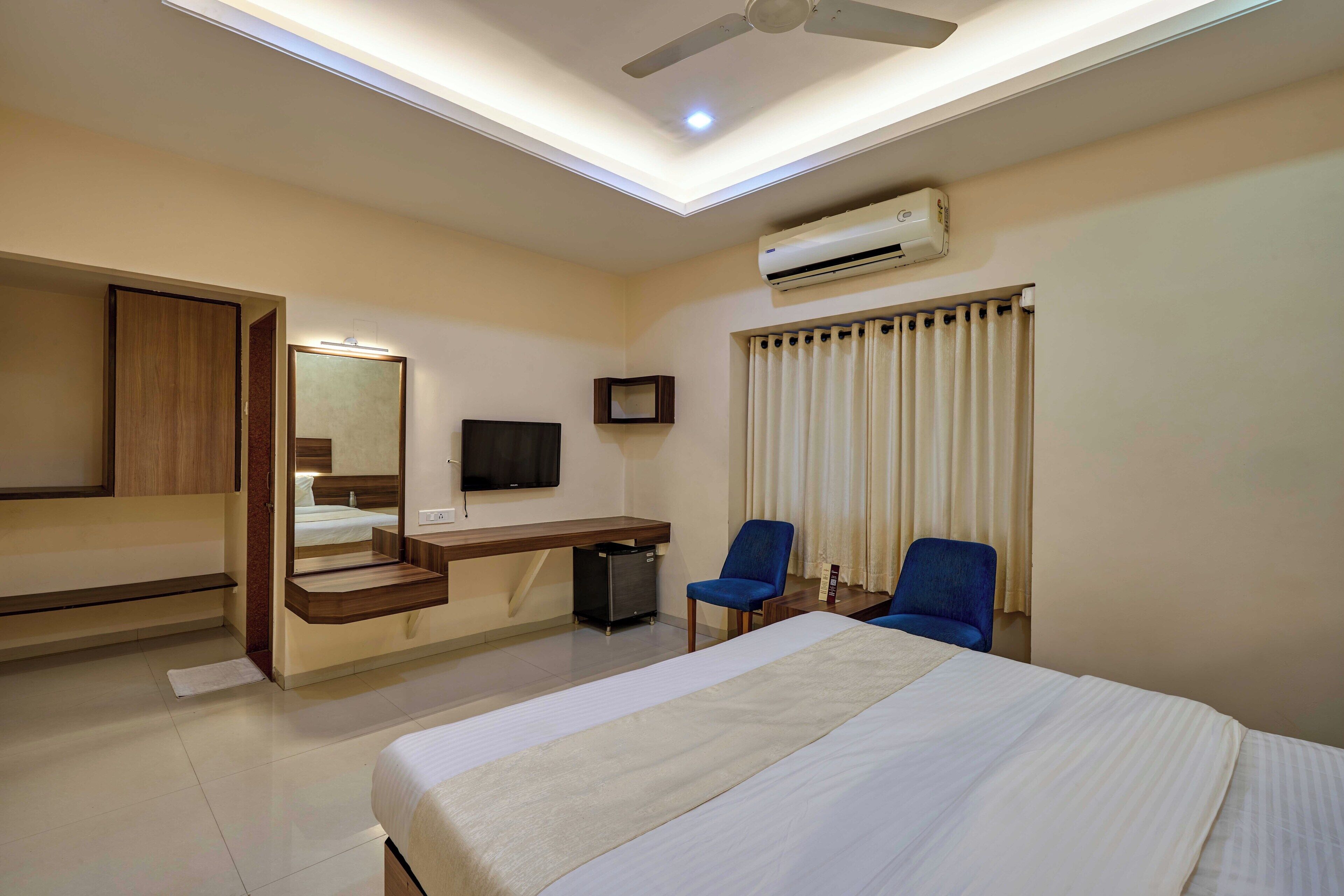 A hotel room with a bed, a desk, a chair, a TV, an air conditioner, and a ceiling fan.