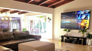 Ein geräumiges Wohnzimmer mit einem großen Flachbildfernseher an der Wand, einem Ledersofa und einem Couchtisch.
