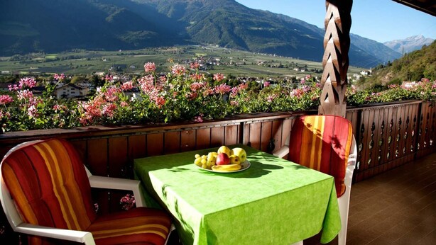 A balcony with a table set for a meal, overlooking a mountainous landscape with a view of a village. - Apartment Weitblick - Alpstay (Naturno)