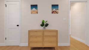 Ein Korridor mit einer weißen Tür, einem Holzschrank mit Schubladen und zwei gerahmten Bildern an der Wand.
