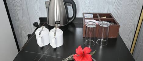 A black marble table with a coffee maker, two white mugs, two glass tumblers, and a red flower.