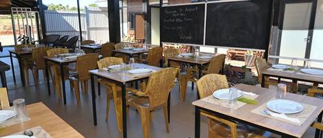 Zona d'esmorzar a l'aire lliure amb taules i cadires, una pissarra amb informació i vista al cel.