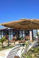 Hotel con mesas al aire libre, sombrilla de paja y vista del exterior.