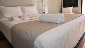 Una cama bien hecha con una toalla enrollada, almohadas blancas y una manta color beige.