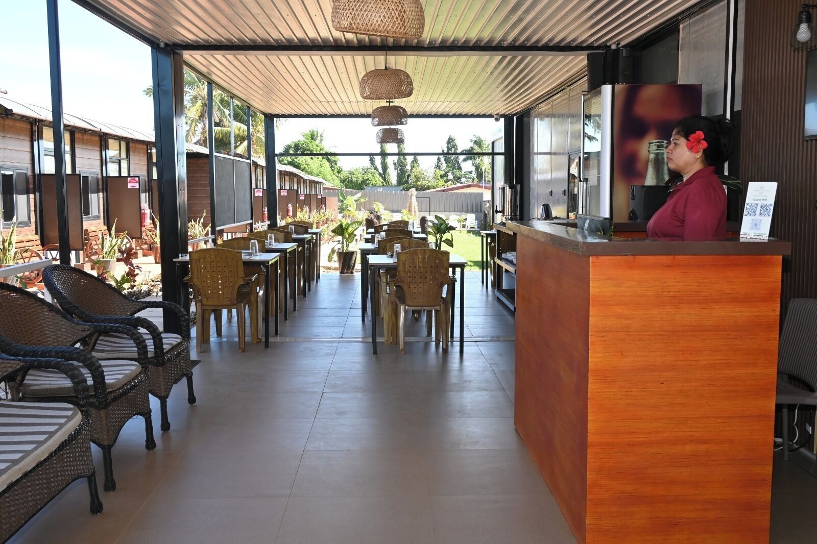 An outdoor cafe with wicker chairs, a wooden reception desk, and potted plants.