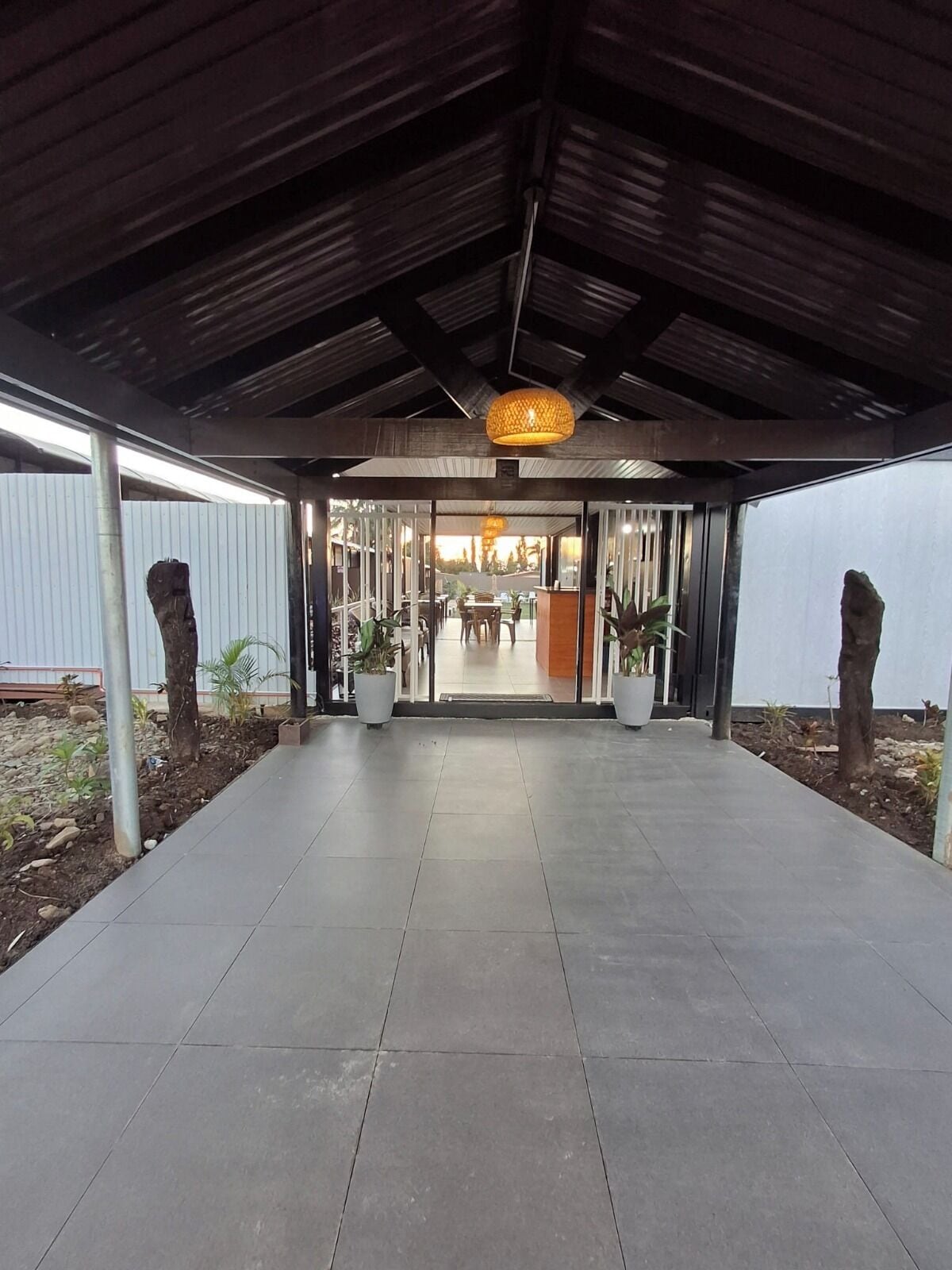 A covered walkway leading to a building with a modern design, featuring a large hanging light fixture and potted plants.
