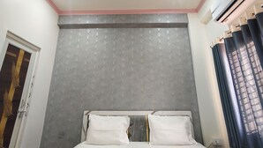 A hotel room with a bed, ceiling fan, air conditioning unit, and a door with decorative panels. - Hotel Shiv Sagar  (Varanasi)