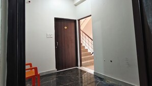 A hallway with a dark wooden door, a red chair, and a staircase leading to an upper level. - Hotel Shiv Sagar  (Varanasi)