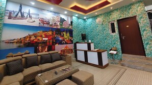 A hotel lobby with a reception desk, seating area, and a mural of a cityscape. - Hotel Shiv Sagar  (Varanasi)