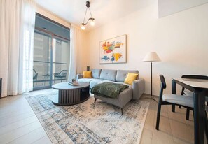 A modern living room with a sofa, a round coffee table, and a dining area with chairs. - Wilton Terrace Apt w/ Pool, Gym & Balcony (Dubai)