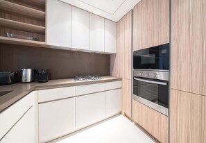 A modern kitchen with white cabinetry, stainless steel appliances, and a wooden accent wall. - Wilton Terrace Apt w/ Pool, Gym & Balcony (Dubai)
