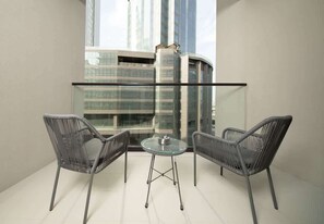 Ein Balkon mit zwei Stühlen und einem Glastisch, der auf einen Stadtblick mit modernen Gebäuden blickt.