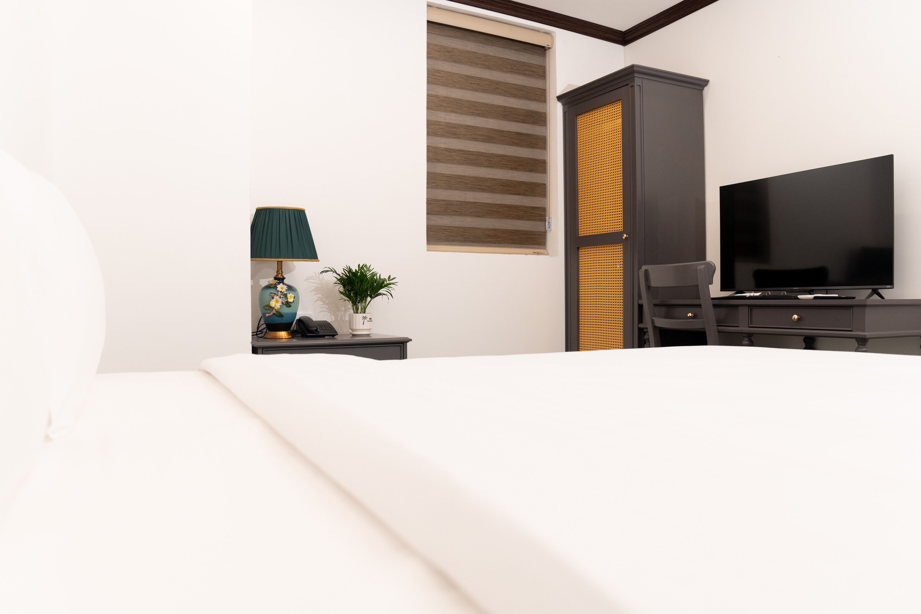 A hotel room with a bed, a desk with a lamp, a television, and a cabinet.