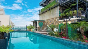 A rooftop pool with a clear view of the city skyline, surrounded by lush greenery and a stone wall.