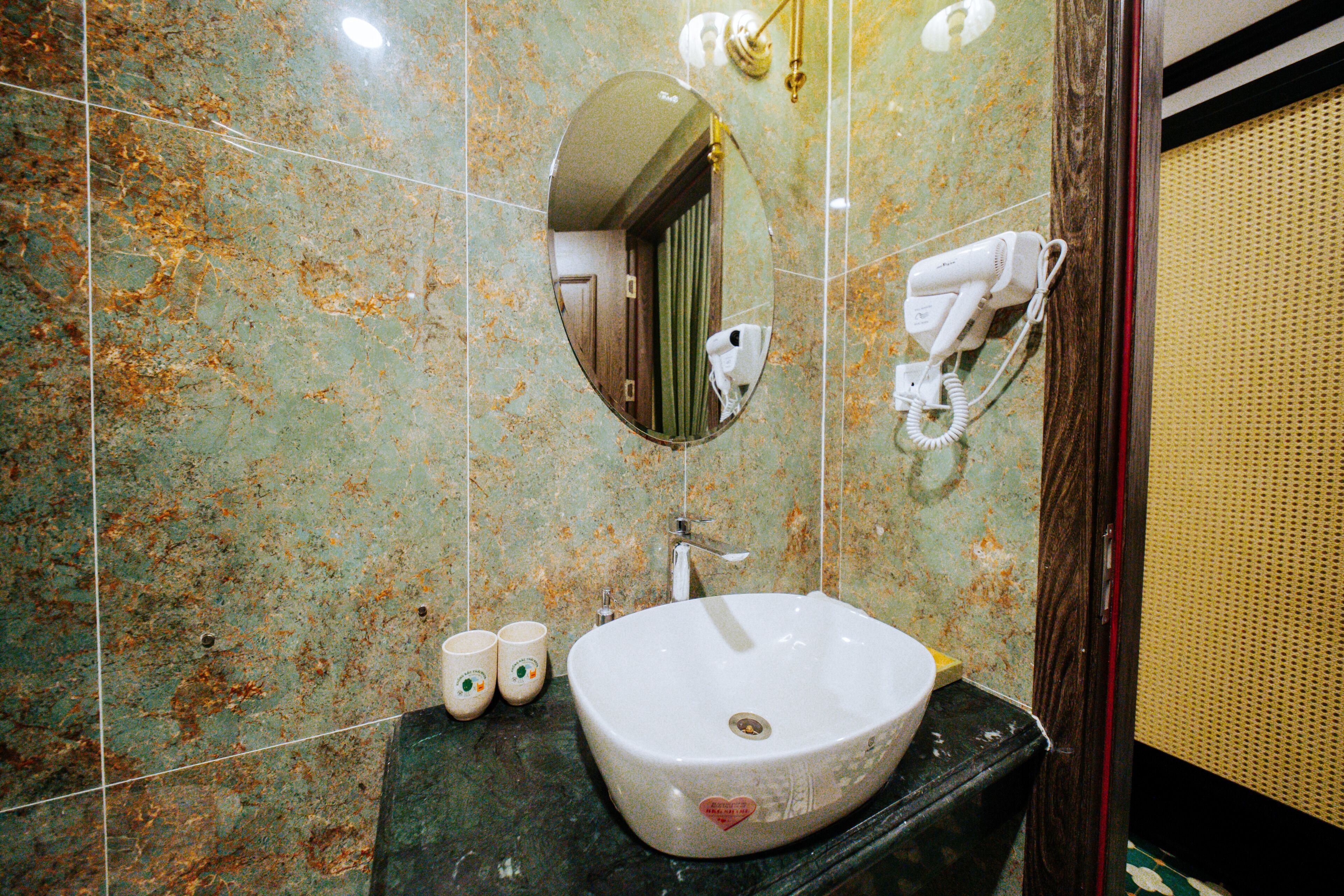 A bathroom with a marble sink, a mirror, and a hairdryer mounted on the wall.