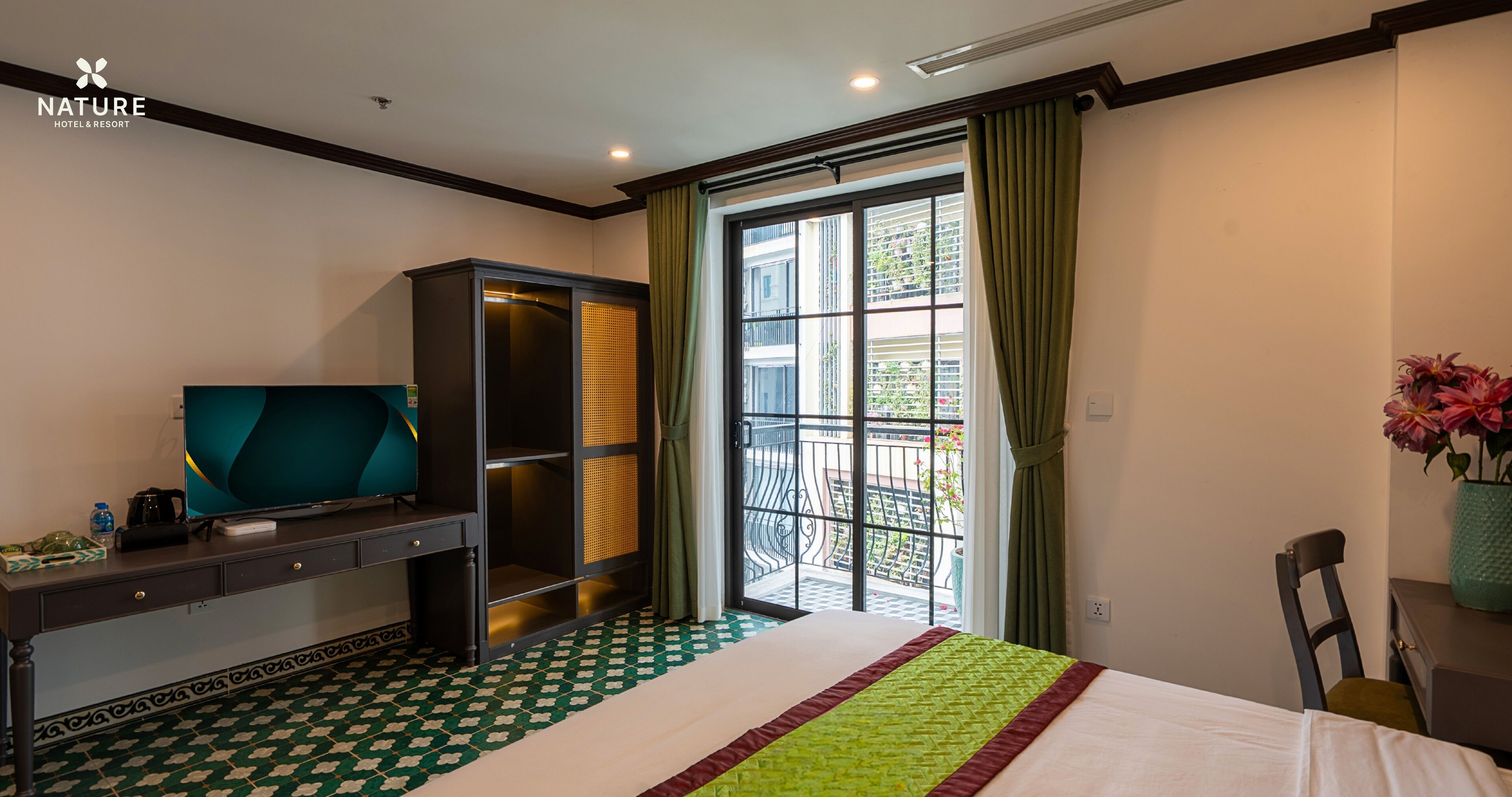 Quarto de hotel com uma cama, uma mesa com televisão, um guarda-roupa e uma varanda com vista para a cidade.