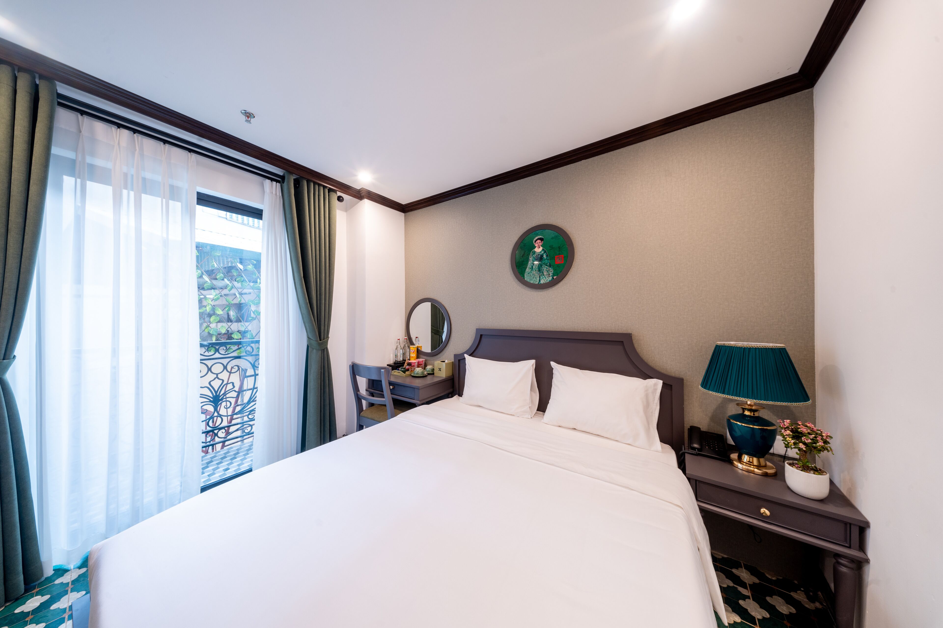 Ein Hotelzimmer mit einem großen Bett, einem Nachttisch mit Lampe und Topfpflanze, einem Schreibtisch mit Stuhl, einem Fenster mit Vorhängen und einem wandmontierten Spiegel.