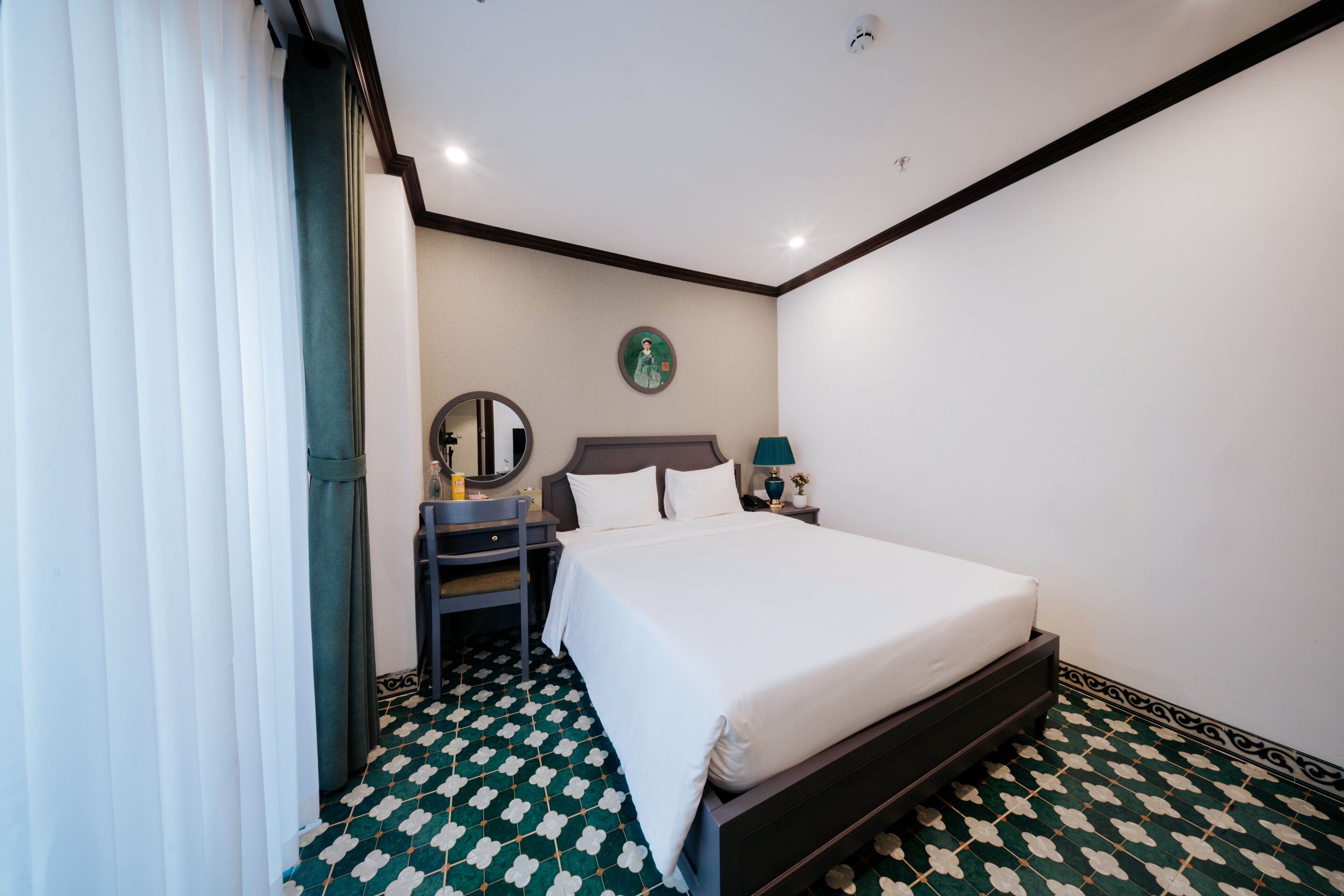 A hotel room with a bed, a desk, a chair, a mirror, and a wall clock.