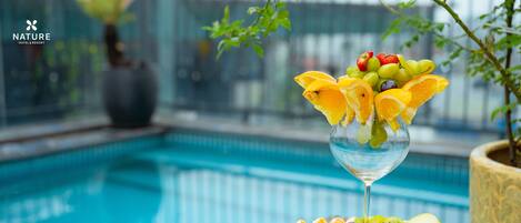 A poolside setting with a fruit and cheese platter and a glass of white wine.