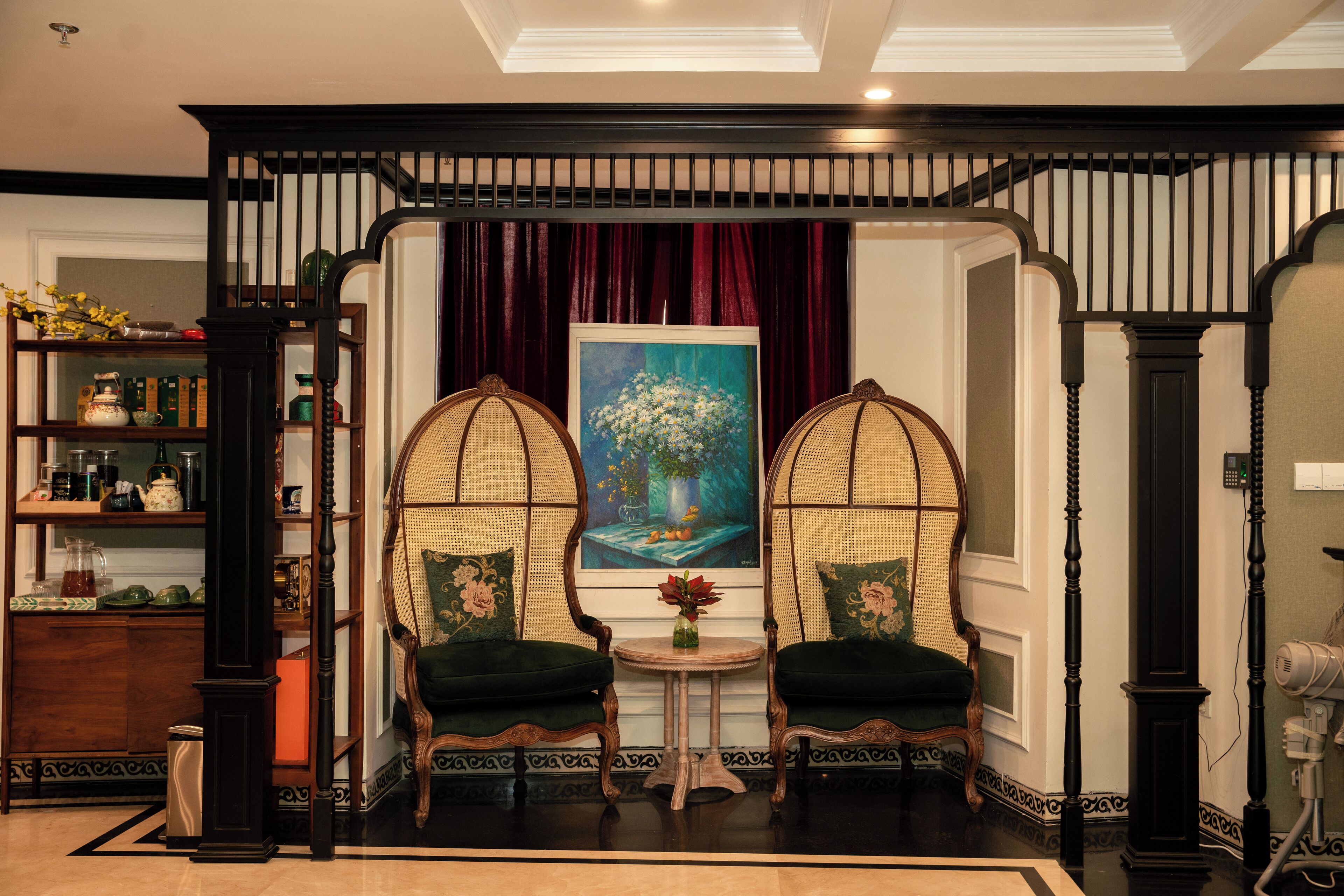 Een kamer met een klassiek interieur, met een houten stoel met een gevlochten rugleuning, een klein rond tafeltje met een vaas en een boekenplank vol boeken en decoratieve objecten.