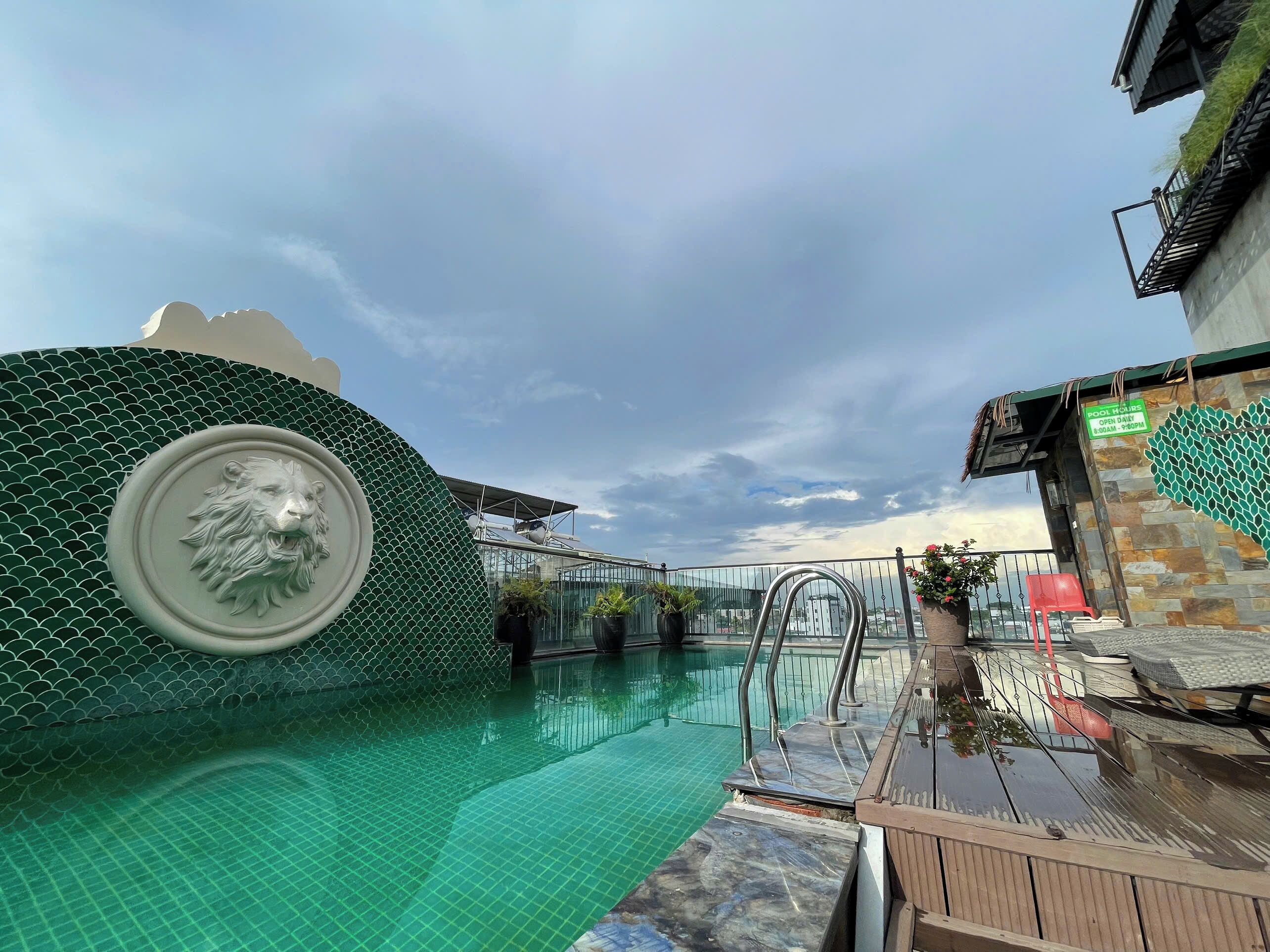 A swimming pool with a lion head sculpture, a glass railing, and a sign indicating pool hours.