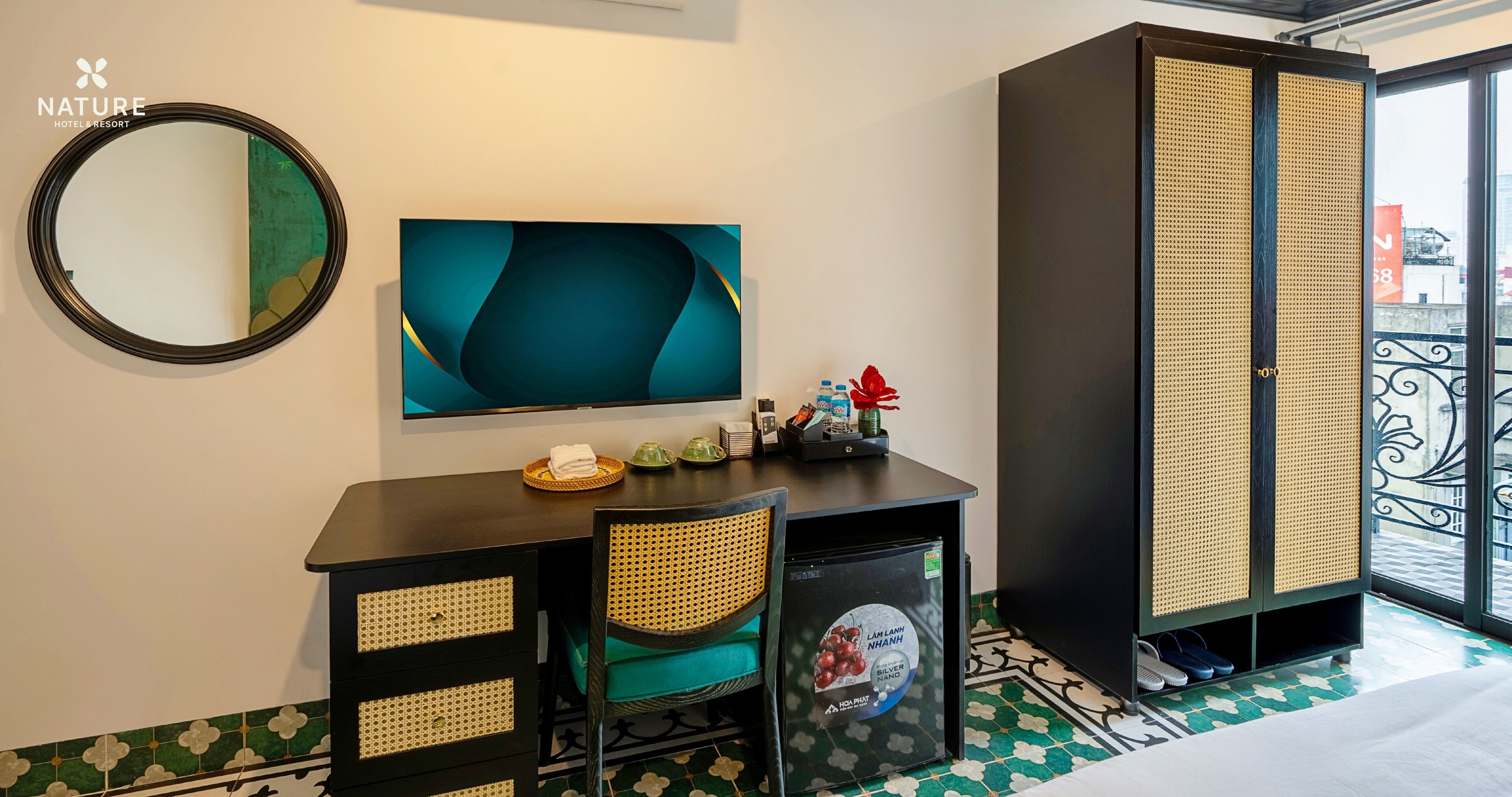 Hotelkamer met een bed, een bureau met stoel, een kleine koelkast, een spiegel, een televisie en een kledingkast.