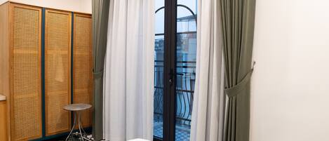 A hotel room with a bed, a small round table, a wooden wardrobe, and a balcony with a checkered floor.