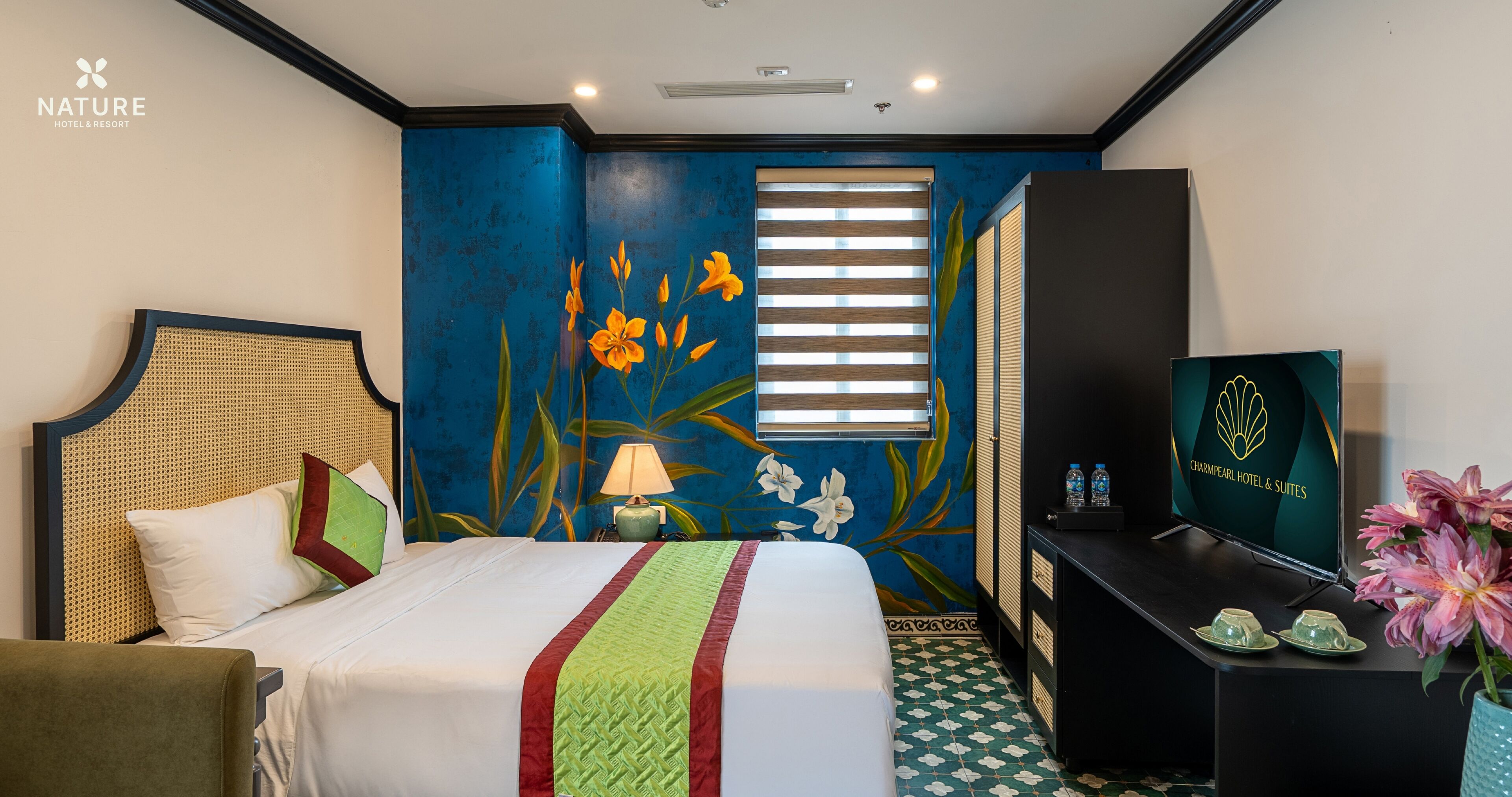 A hotel room with a bed, a desk, a TV, and a window with blinds.