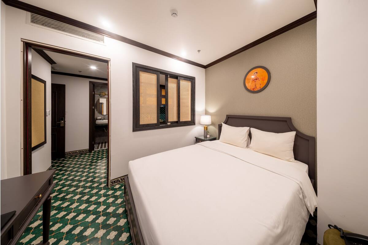 Una habitación de hotel con cama, mesita de noche, lámpara y un reloj de pared.