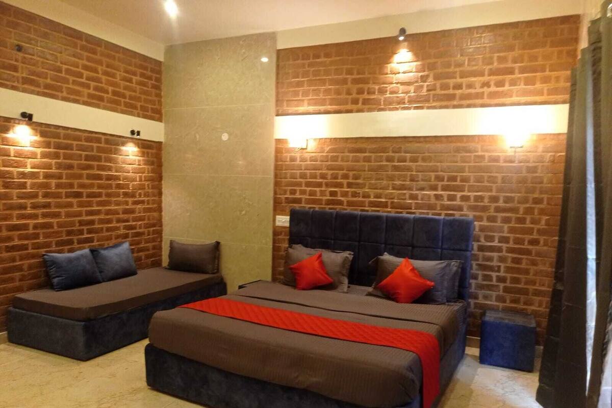 Une pièce avec un mur en briques, un lit avec une tête de lit, deux coins salon et un luminaire.