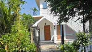 A modern two-story house with a wooden door, a staircase leading to the entrance, and a well-maintained lawn. - Athulya Resort – Leisure and Luxury cottages from EMBEHolidays (Cheyyur)